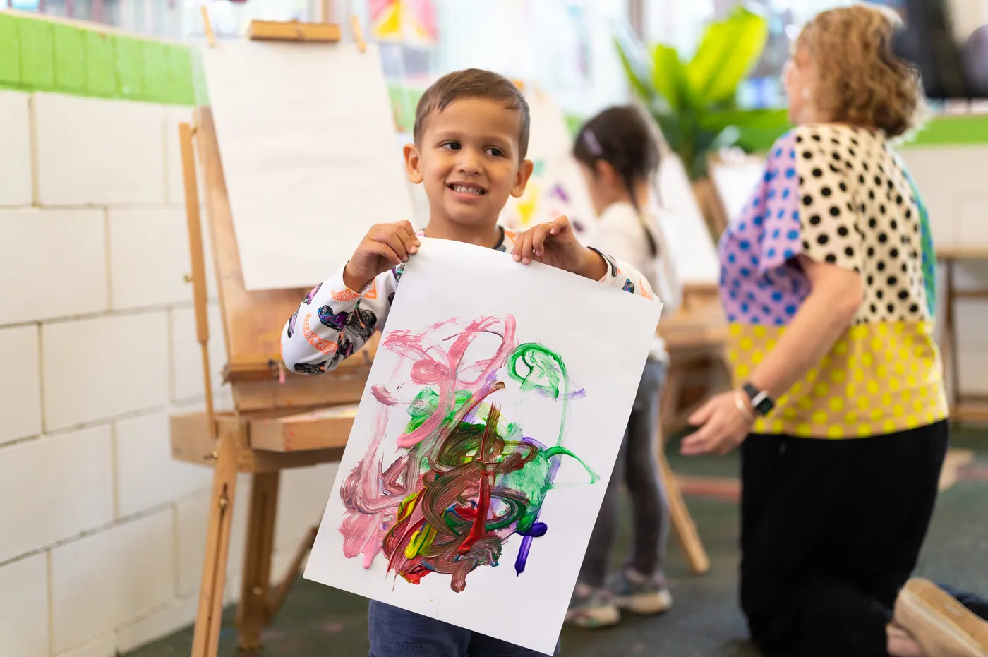 A Grandi child grinning as he holds up the painting he has just finished