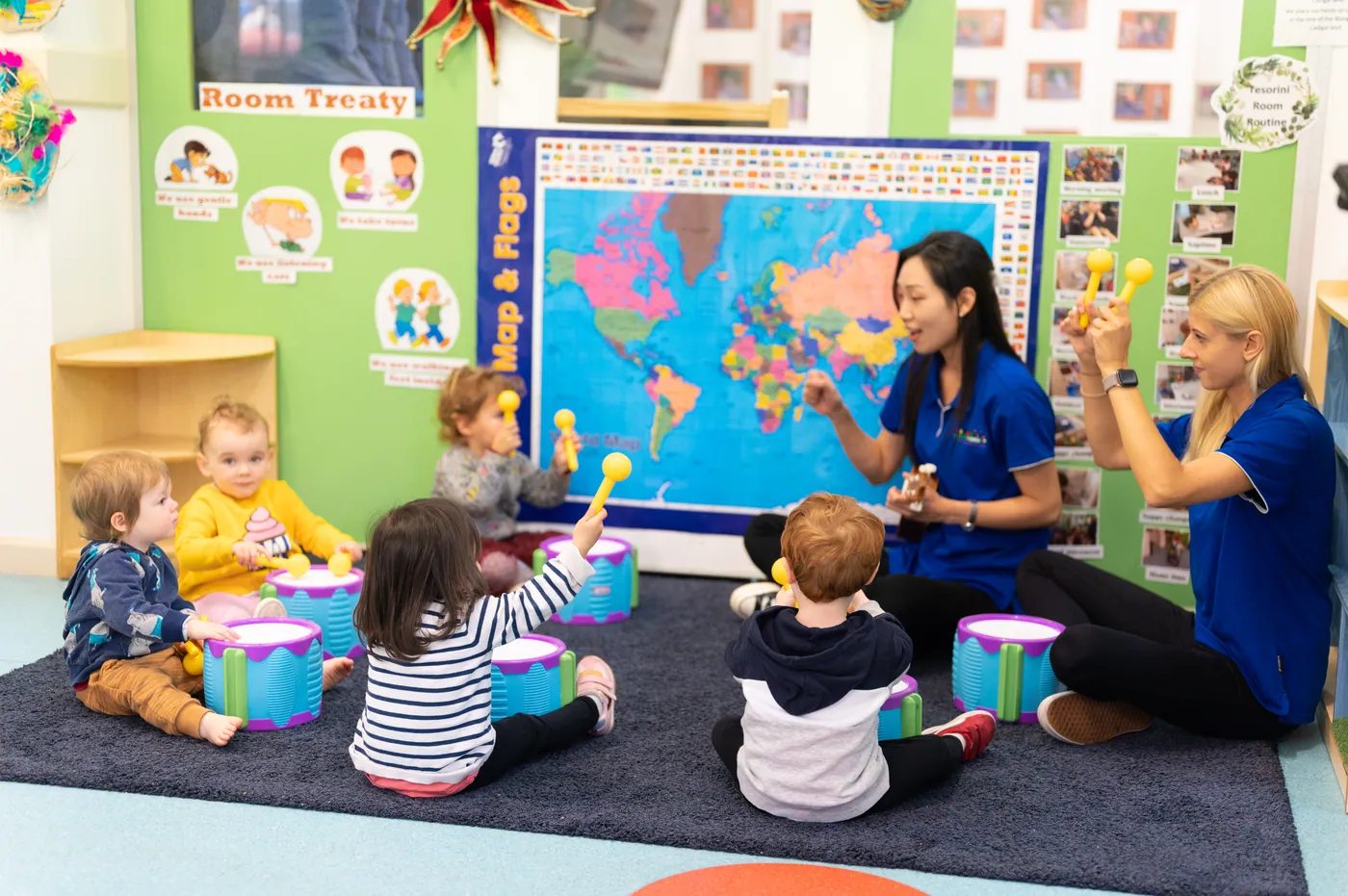 Babies and toddlers sitting with drums while an educator leads a music circle