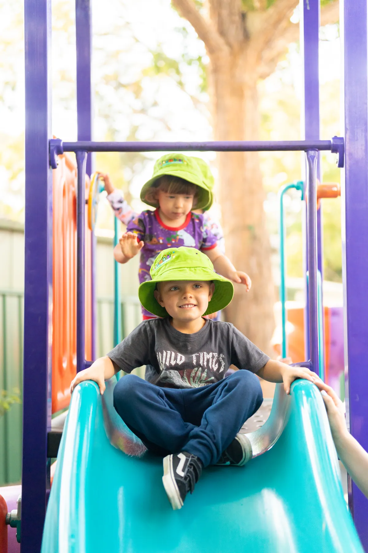 A preschooler coming down the playground slide with a friend close behind