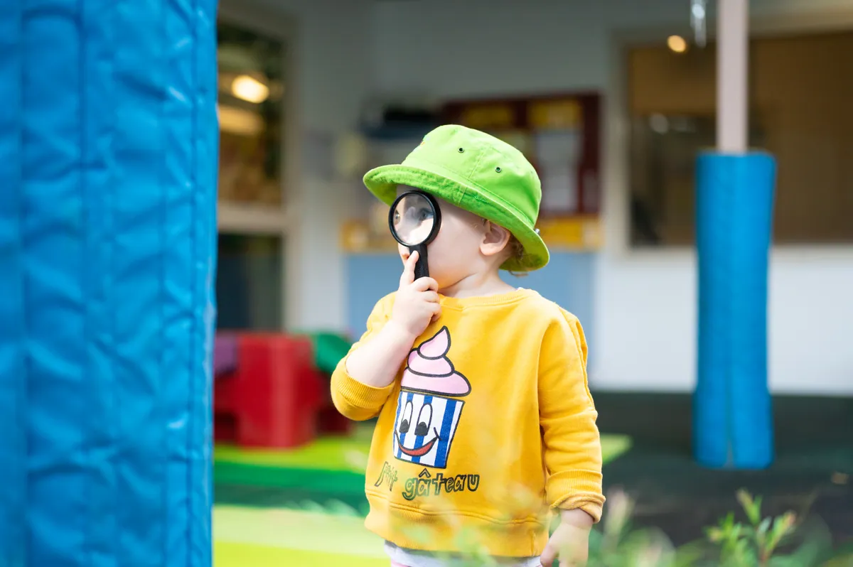A toddler exploring the outdoor play area with a magnifying glass