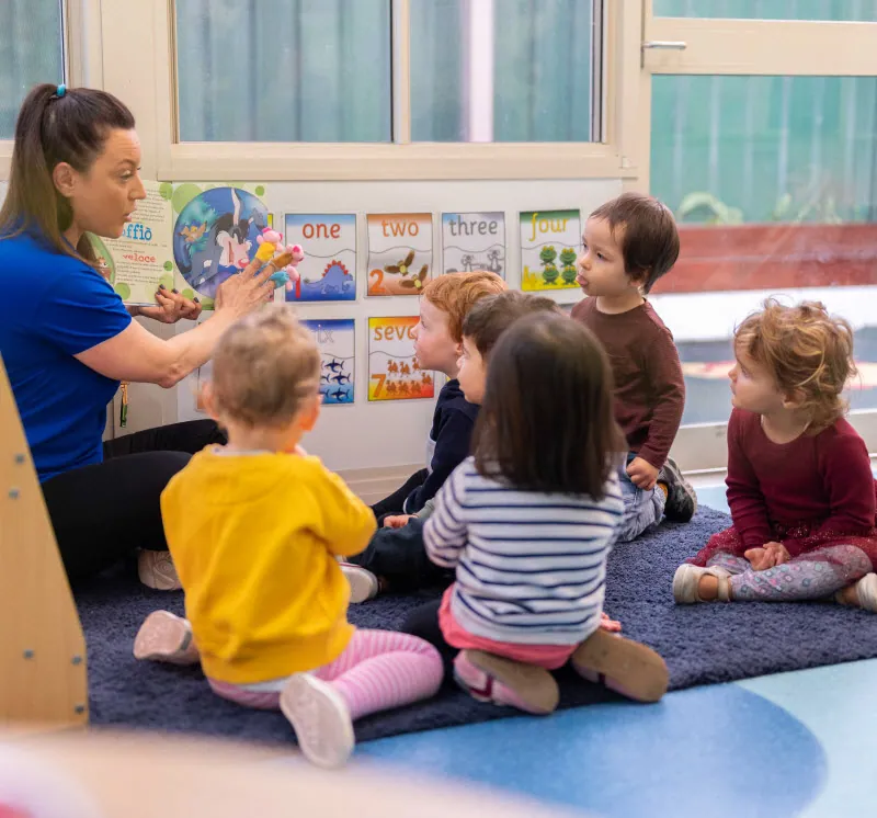 An educator sitting with a group of toddlers in front of a wall of number cards