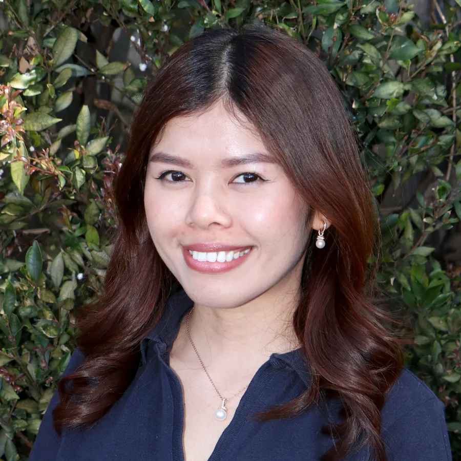 Grace smiling to camera, long auburn hair and pearl earrings, in Bambini uniform in front of the centre’s green hedge